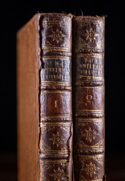 fig 1. A two-volume set of 18th-century leather-bound books featuring gilt-tooled spine details and raised bands standing vertically.