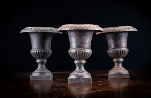 fig 1. A set of three miniature cast iron urns featuring fluted campana bodies and square pedestal bases with a dark patinated finish.