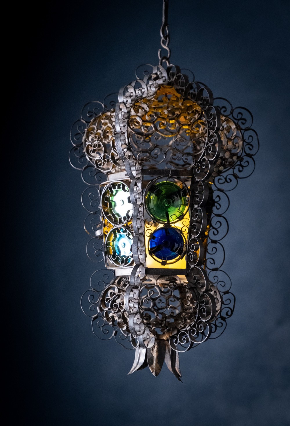 A 19th-century Venetian hanging lantern crafted from intricate wrought iron scrollwork with inset round coloured glass panels in green, blue, and amber.