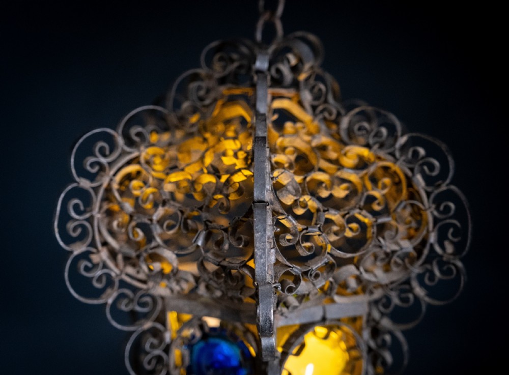 A 19th-century Venetian hanging lantern crafted from intricate wrought iron scrollwork with inset round coloured glass panels in green, blue, and amber. View IV