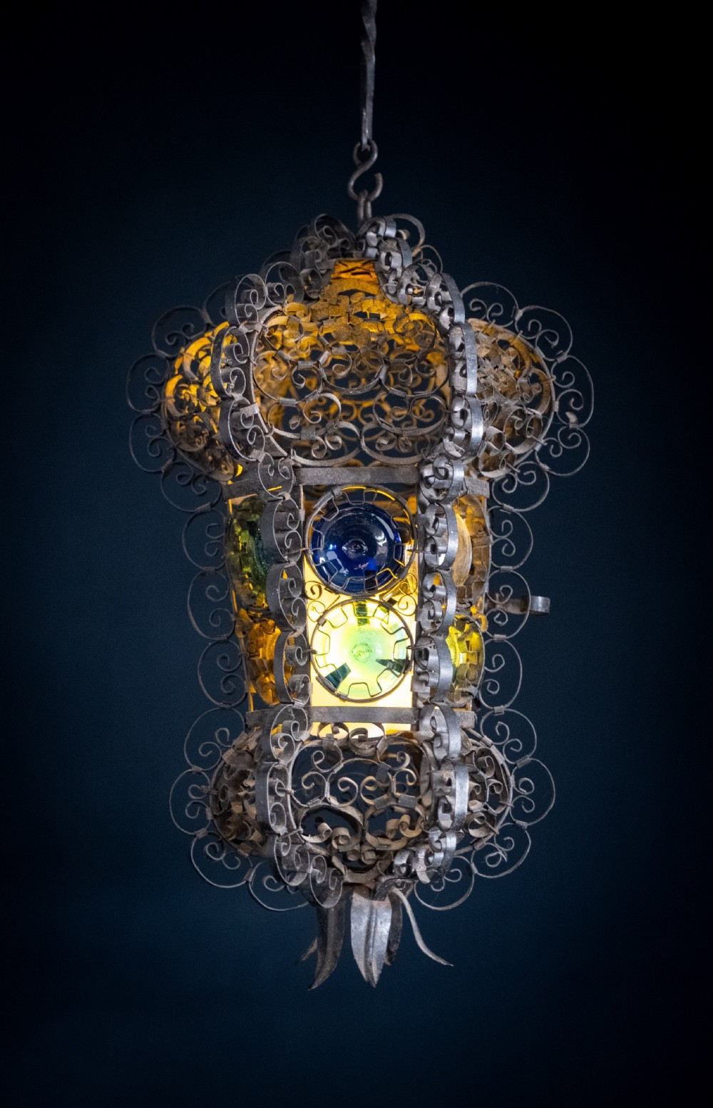 A 19th-century Venetian hanging lantern crafted from intricate wrought iron scrollwork with inset round coloured glass panels in green, blue, and amber. View V