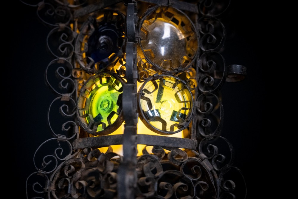 A 19th-century Venetian hanging lantern crafted from intricate wrought iron scrollwork with inset round coloured glass panels in green, blue, and amber. View VII