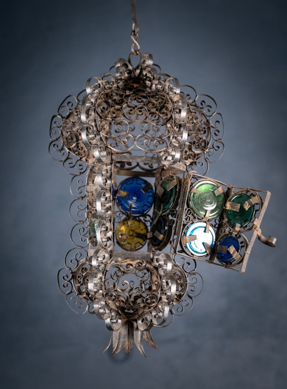 A 19th-century Venetian hanging lantern crafted from intricate wrought iron scrollwork with inset round coloured glass panels in green, blue, and amber. View IX