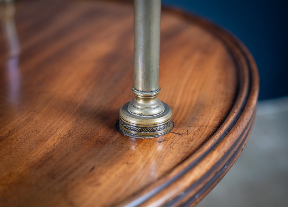 A two-tier Regency mahogany dumb waiter featuring a turned central column, brass uprights, and a tripartite base with castors. View V