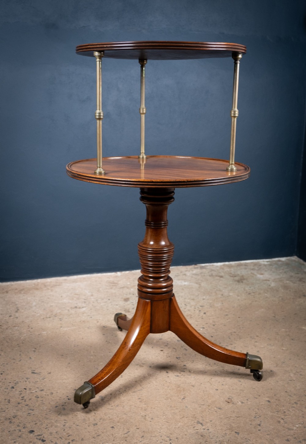 A two-tier Regency mahogany dumb waiter featuring a turned central column, brass uprights, and a tripartite base with castors. View VIII