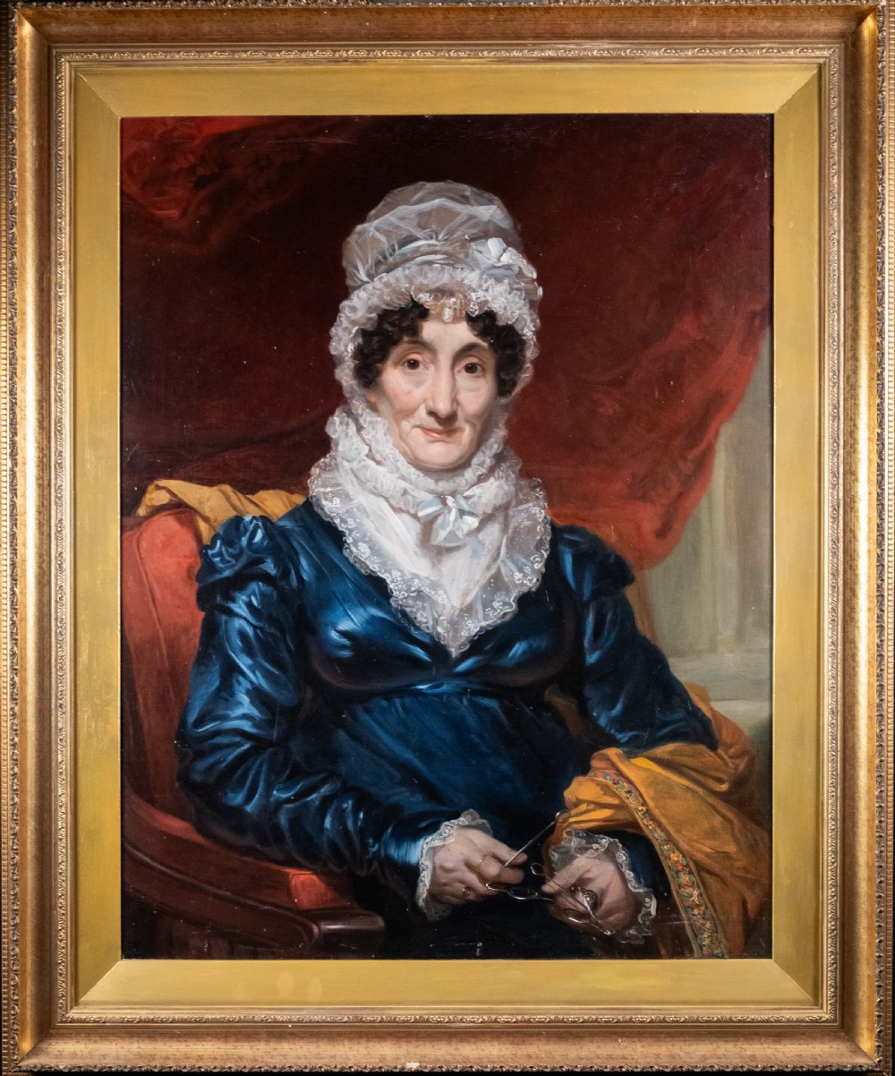 A large antique framed oil painting depicting a seated woman wearing a blue dress and white lace cap against a dark red backdrop.