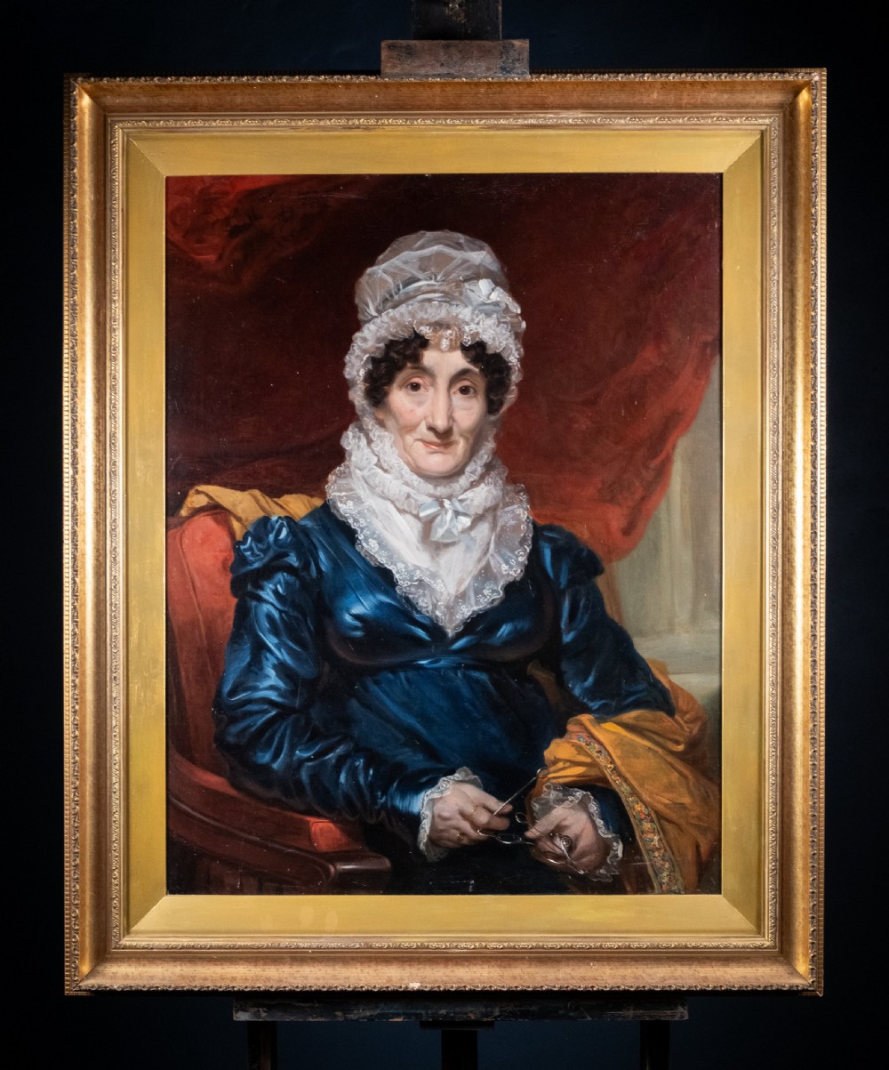A large antique framed oil painting depicting a seated woman wearing a blue dress and white lace cap against a dark red backdrop. View VII