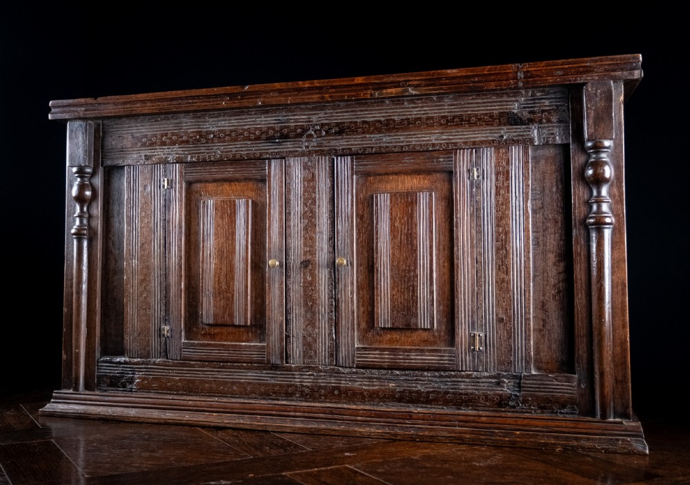 A rectangular eighteenth-century oak wall cupboard featuring double panelled doors, geometric mouldings, and turned corner columns.