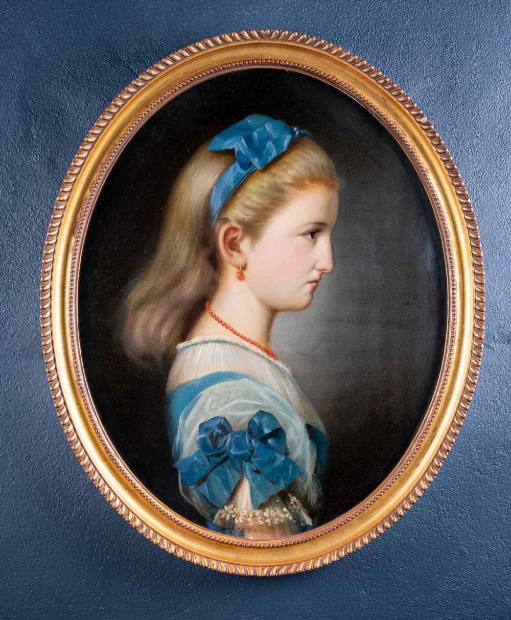 An oval 19th-century oil painting depicting the profile of a young girl wearing a blue dress and hair ribbon, enclosed in an ornate gold frame.