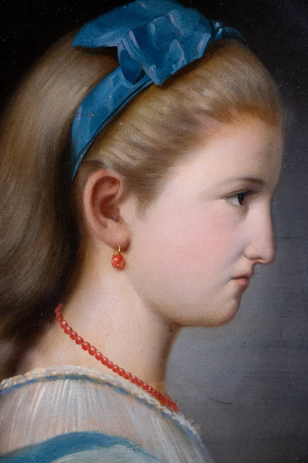An oval 19th-century oil painting depicting the profile of a young girl wearing a blue dress and hair ribbon, enclosed in an ornate gold frame. View II