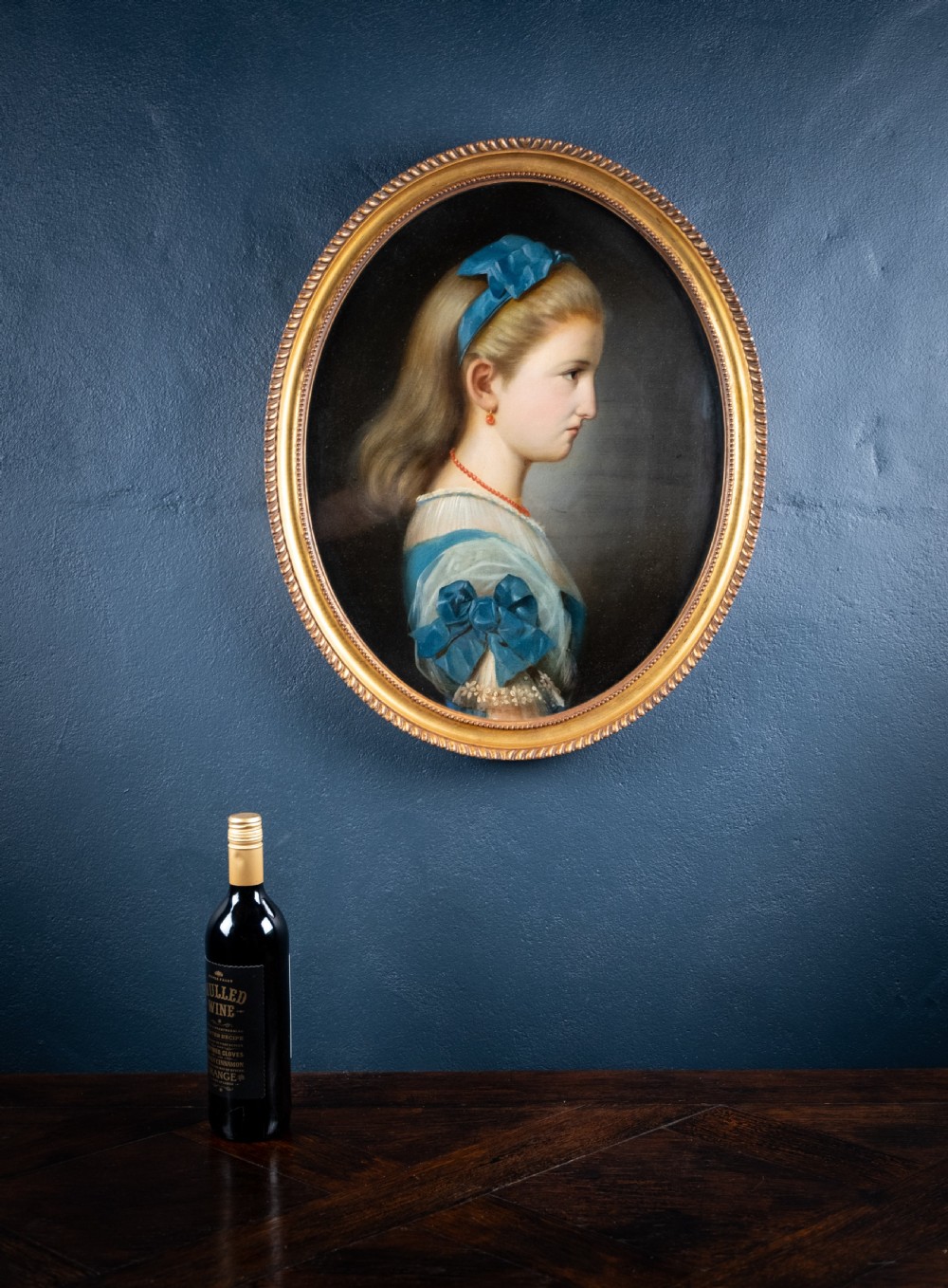 An oval 19th-century oil painting depicting the profile of a young girl wearing a blue dress and hair ribbon, enclosed in an ornate gold frame. View VII