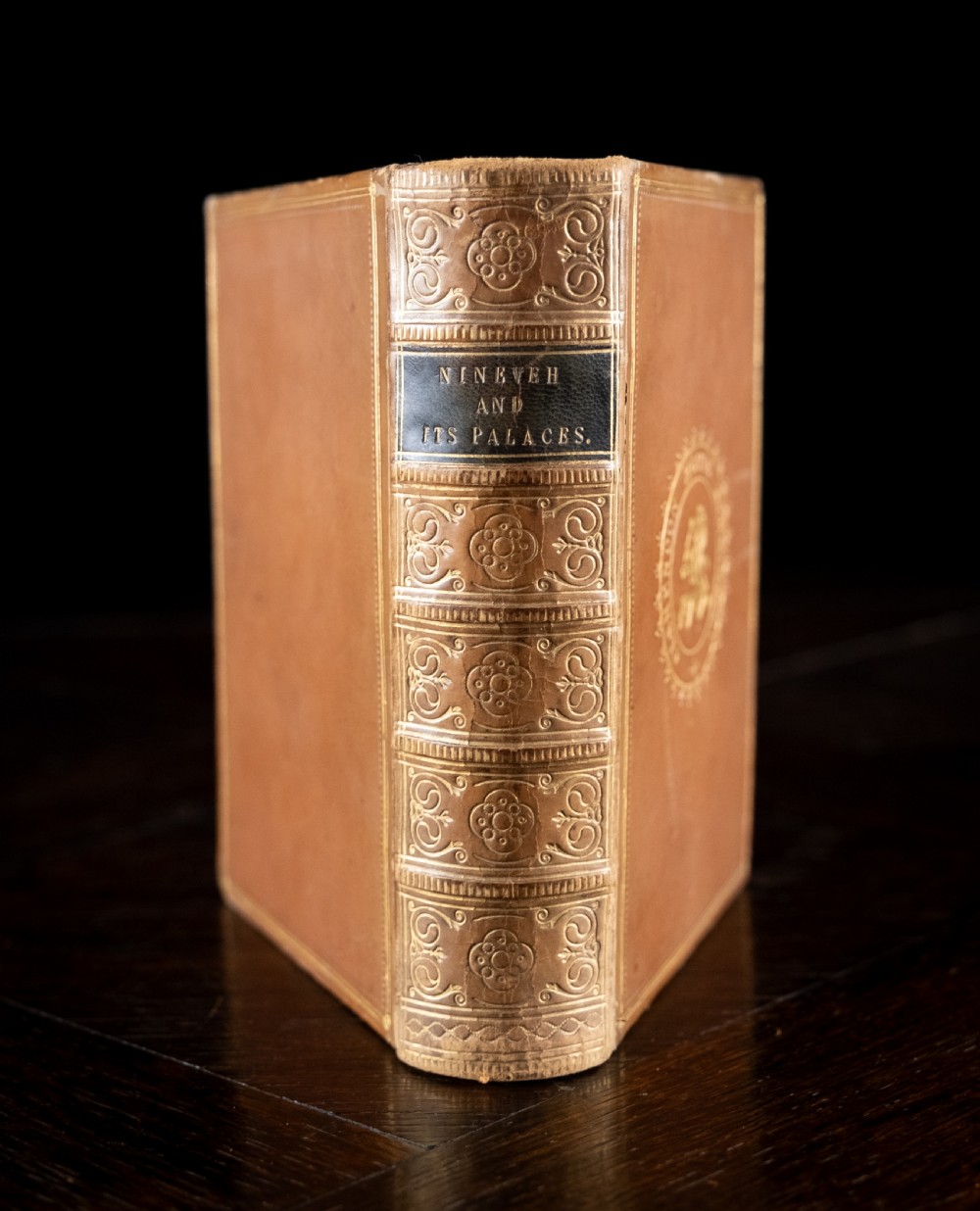 An 1857 tan leather-bound book titled Nineveh and Its Palaces featuring a gilded spine with raised bands and blind-tooled decoration.