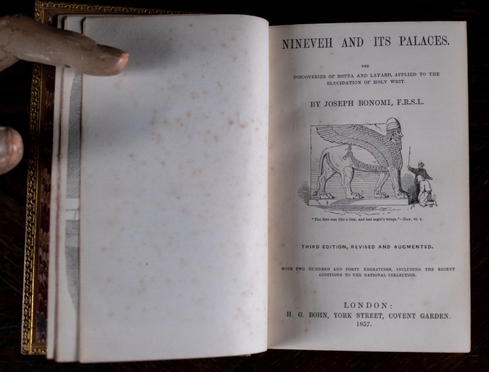 An 1857 tan leather-bound book titled Nineveh and Its Palaces featuring a gilded spine with raised bands and blind-tooled decoration. View XI