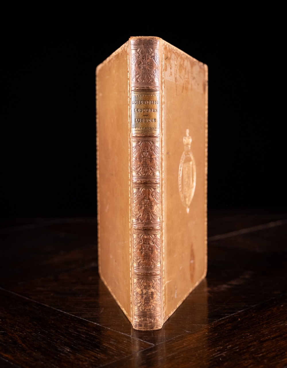 A nineteenth-century tan leather-bound book featuring ornate gilt tooling on the spine and an embossed coat of arms on the front cover.