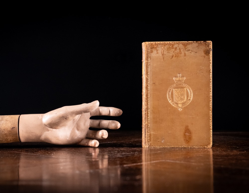 A nineteenth-century tan leather-bound book featuring ornate gilt tooling on the spine and an embossed coat of arms on the front cover. View XIII