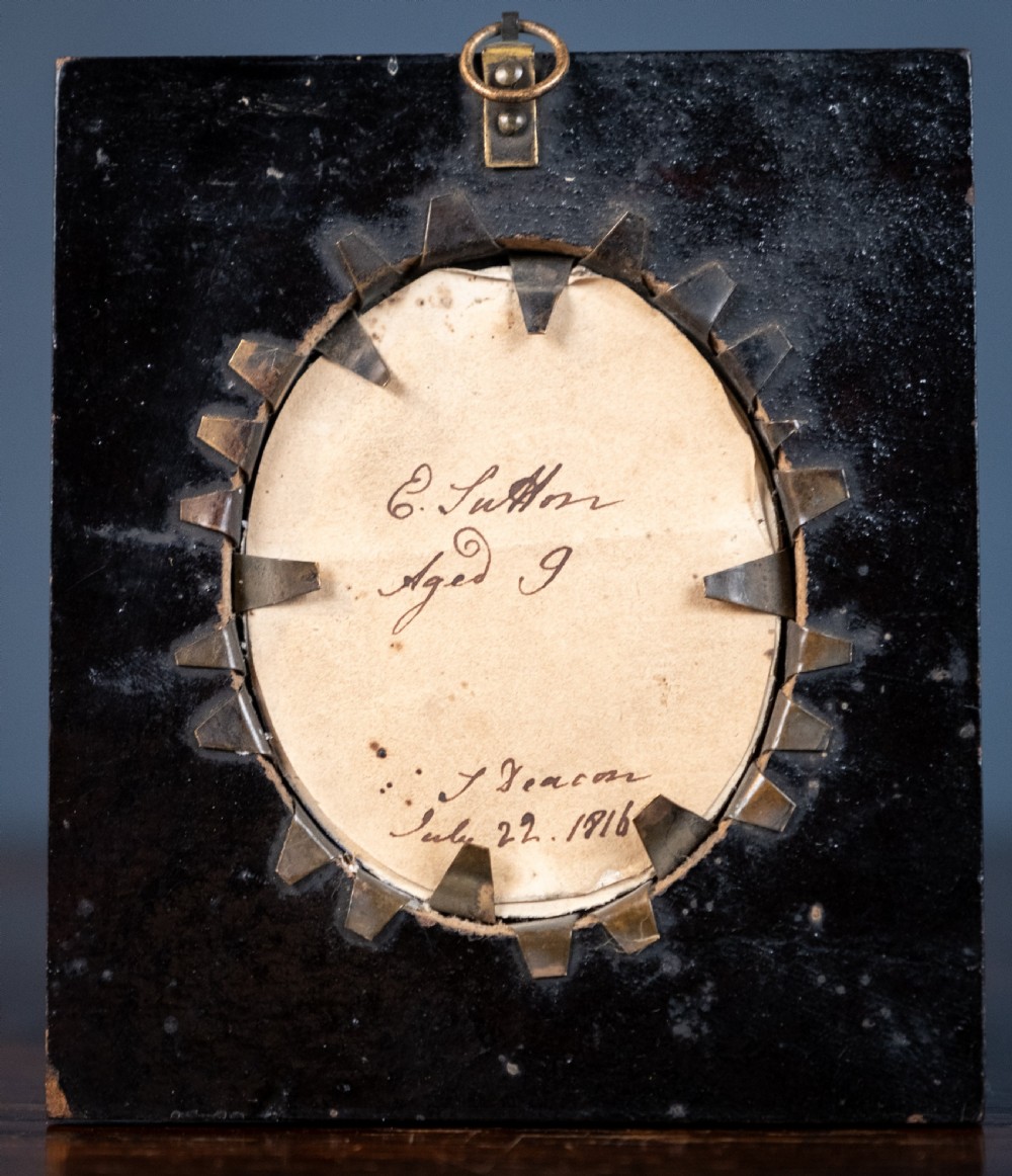 A small oval silhouette portrait of a profile with gilded details, enclosed in a brass oval bezel inside a black rectangular papier-mache frame with a brass floral hanger. View IV