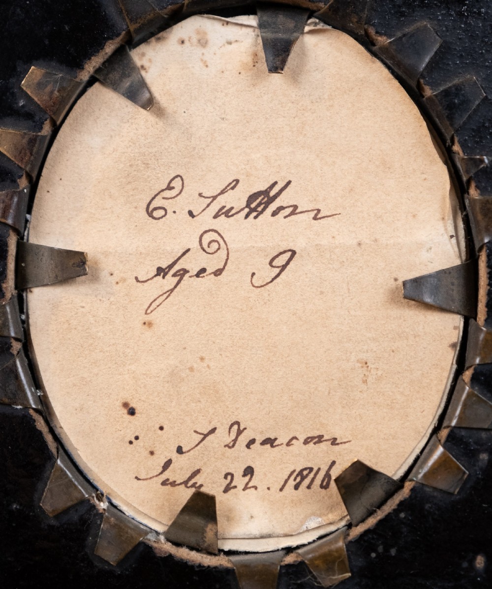 A small oval silhouette portrait of a profile with gilded details, enclosed in a brass oval bezel inside a black rectangular papier-mache frame with a brass floral hanger. View V