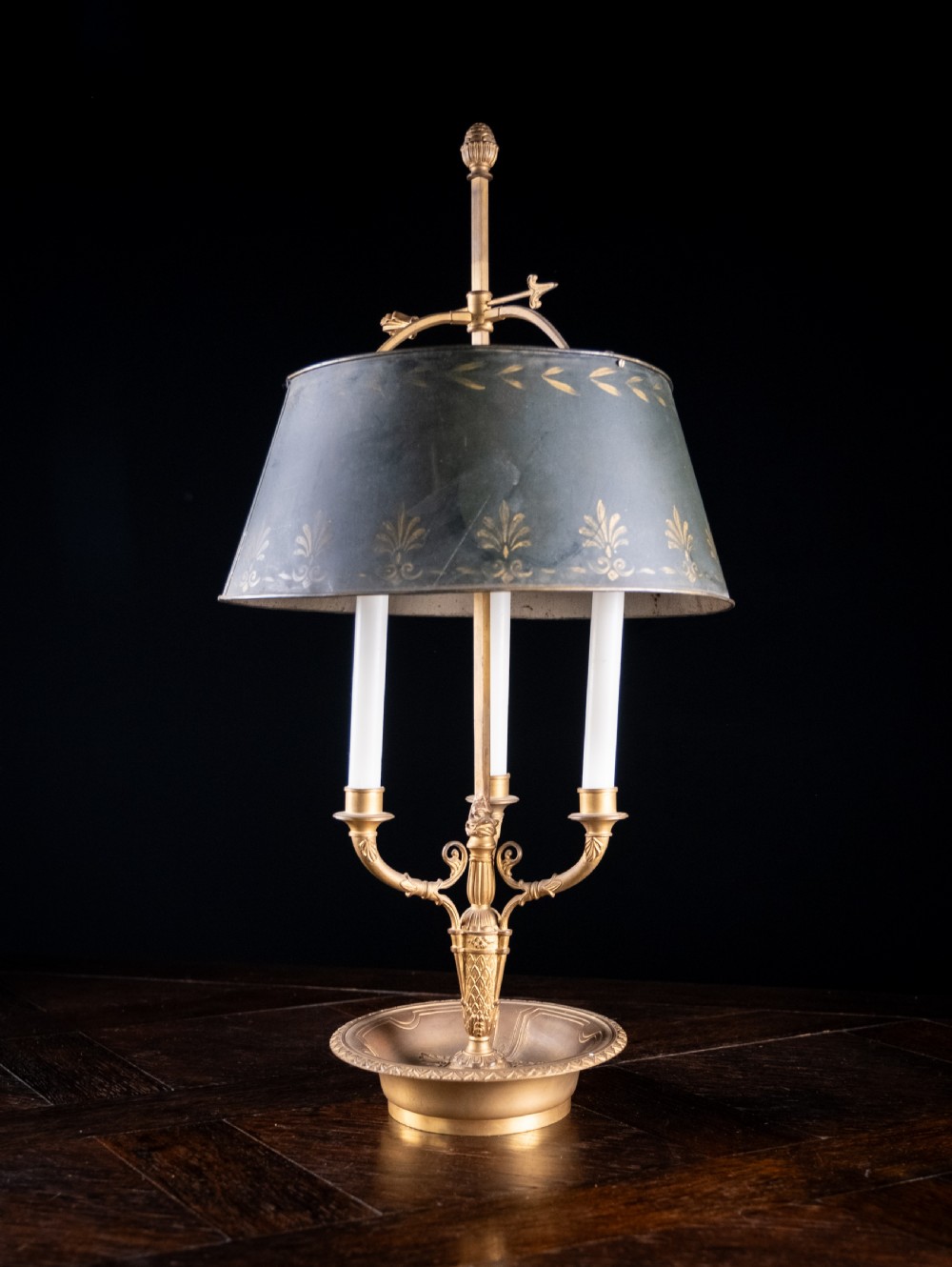 A gilt brass bouillotte lamp featuring a dark adjustable shade and three candle-style lights on a circular tray base.
