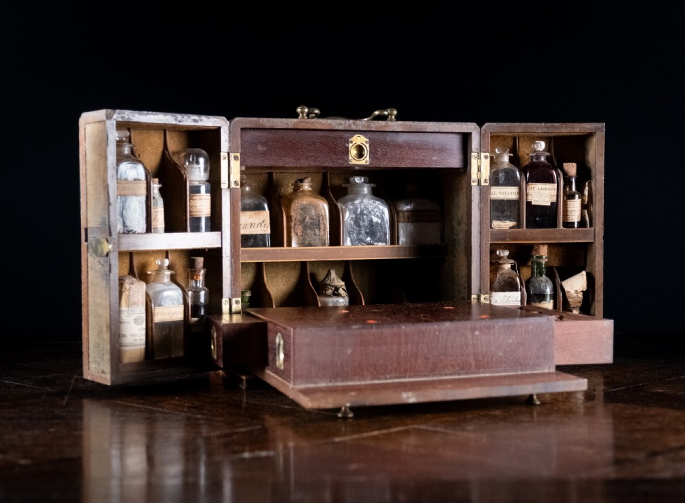An open antique wooden apothecary cabinet featuring multiple compartments filled with vintage glass medicine bottles.