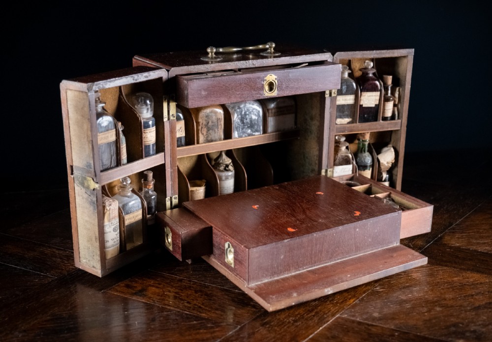 An open antique wooden apothecary cabinet featuring multiple compartments filled with vintage glass medicine bottles. View II