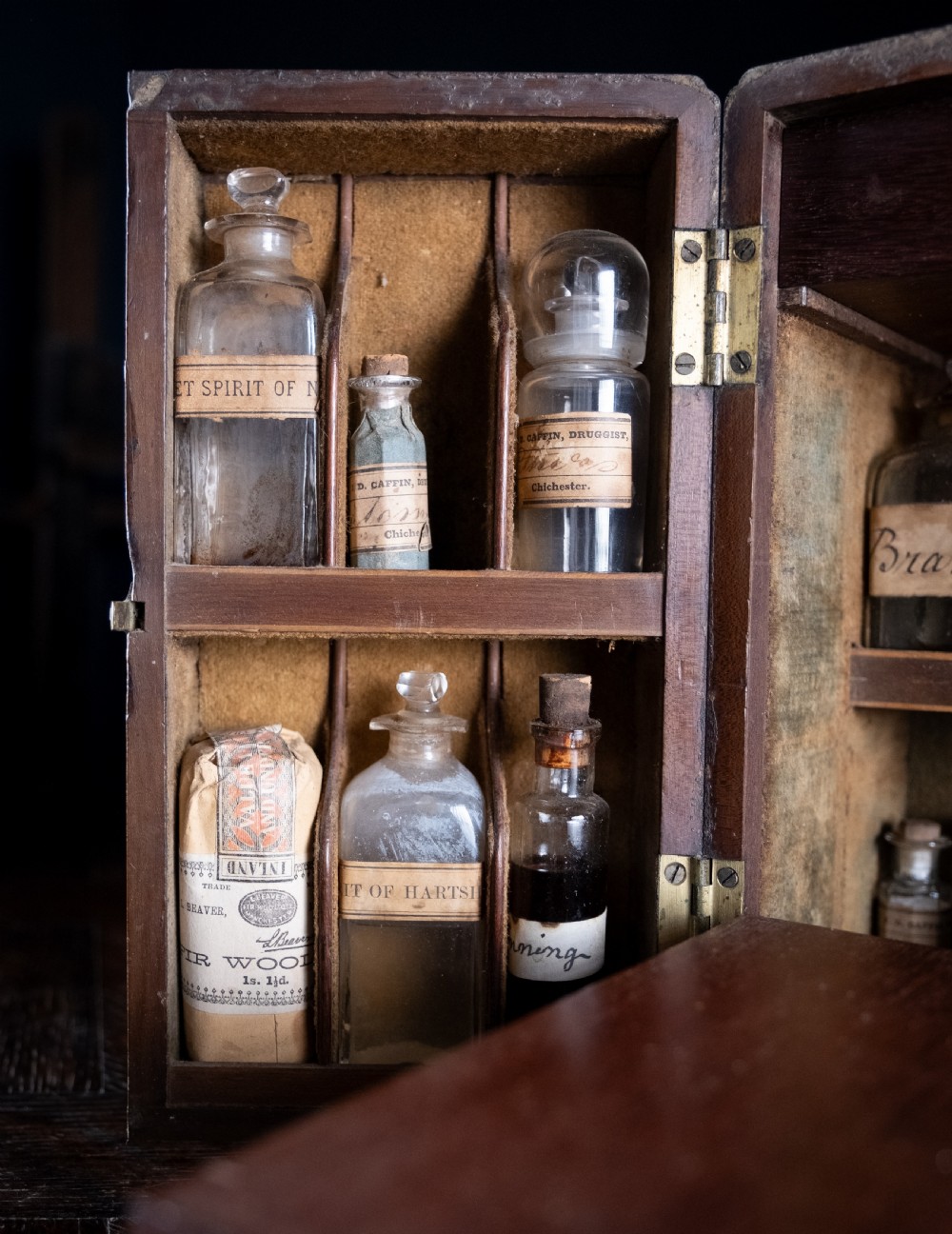 An open antique wooden apothecary cabinet featuring multiple compartments filled with vintage glass medicine bottles. View IV