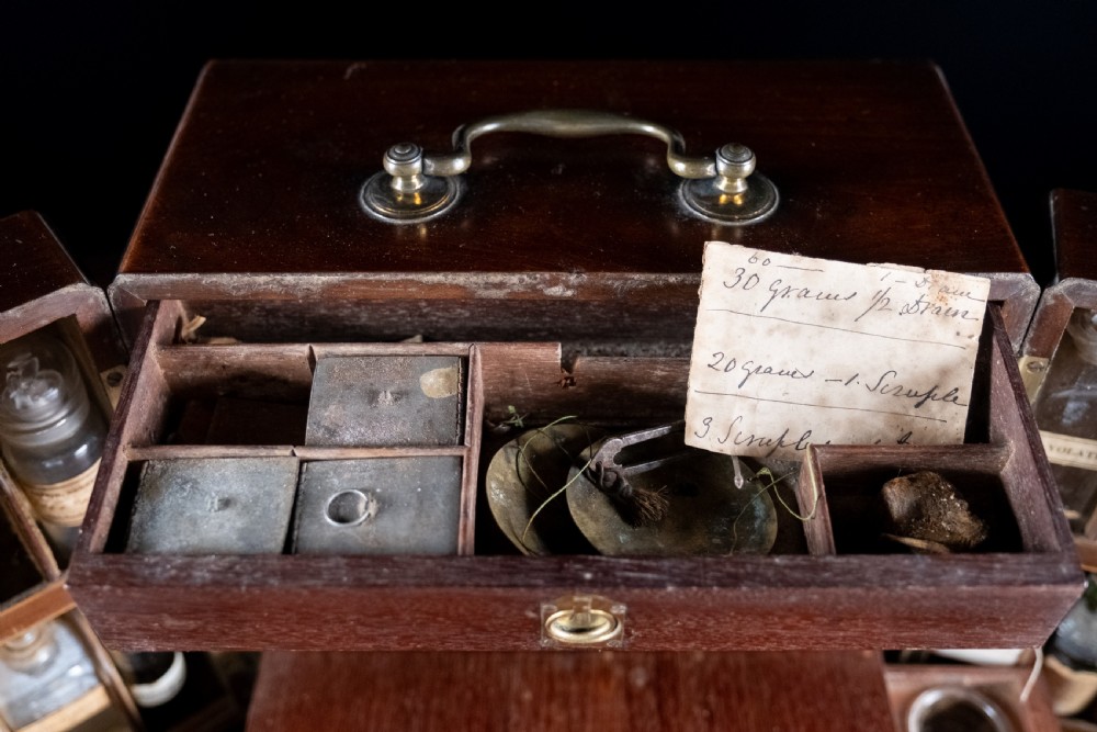 An open antique wooden apothecary cabinet featuring multiple compartments filled with vintage glass medicine bottles. View VII