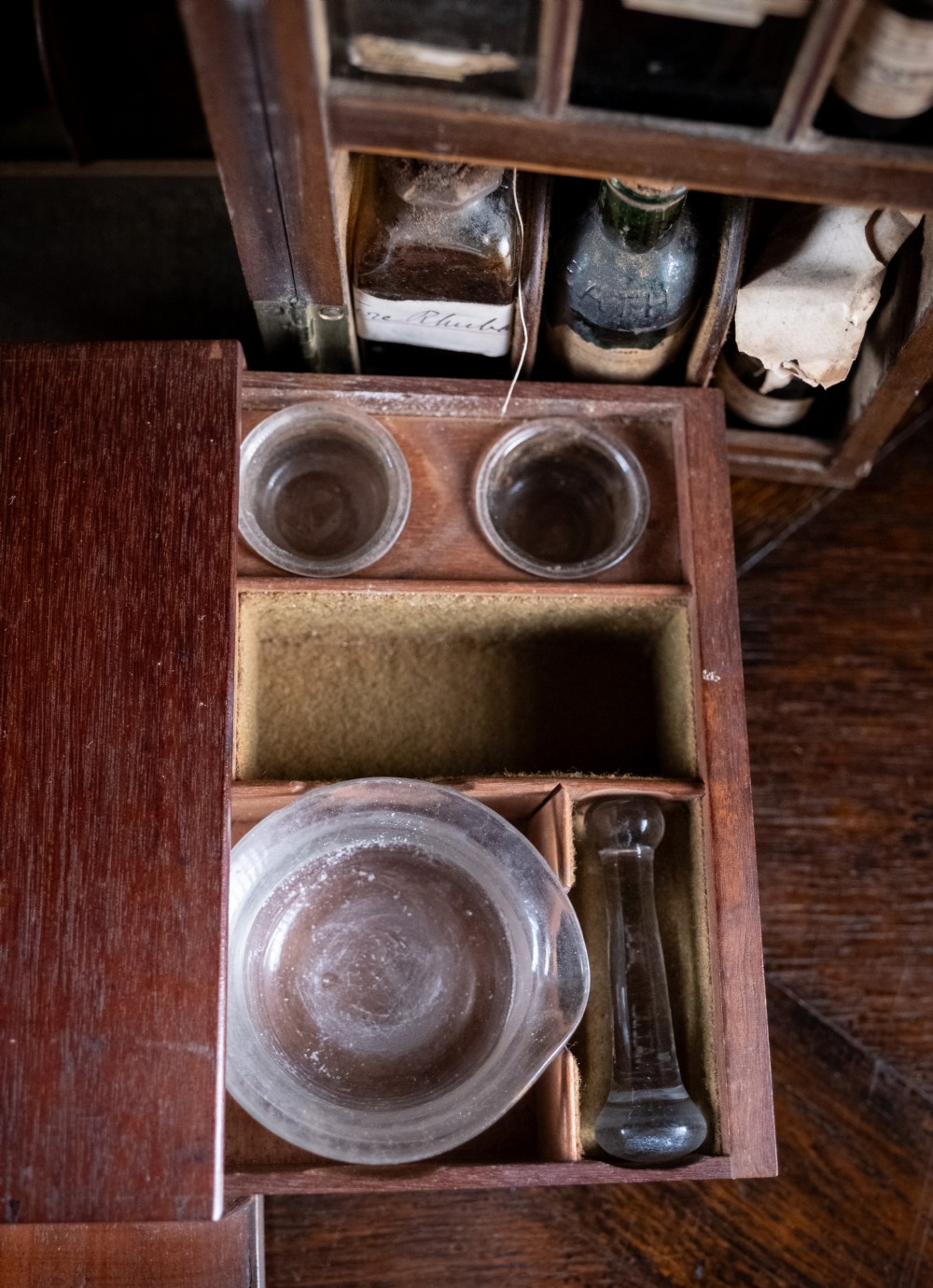 An open antique wooden apothecary cabinet featuring multiple compartments filled with vintage glass medicine bottles. View VIII