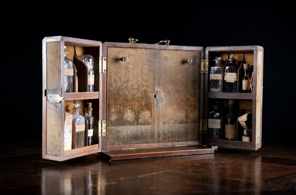 An open antique wooden apothecary cabinet featuring multiple compartments filled with vintage glass medicine bottles. View XII