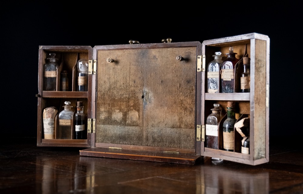 An open antique wooden apothecary cabinet featuring multiple compartments filled with vintage glass medicine bottles. View XIII