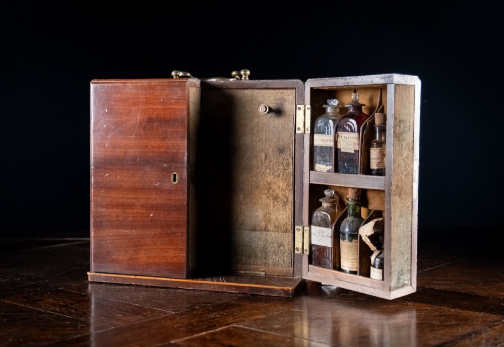 An open antique wooden apothecary cabinet featuring multiple compartments filled with vintage glass medicine bottles. View XIV