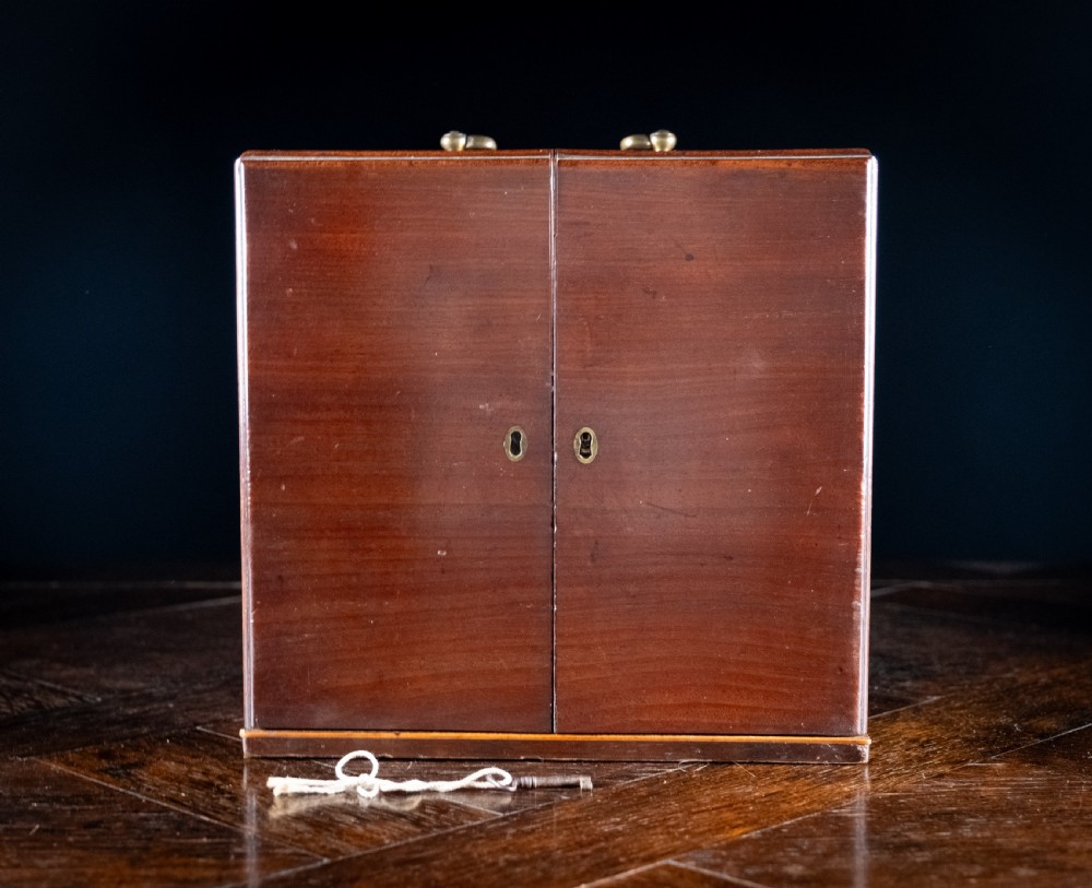An open antique wooden apothecary cabinet featuring multiple compartments filled with vintage glass medicine bottles. View XVII