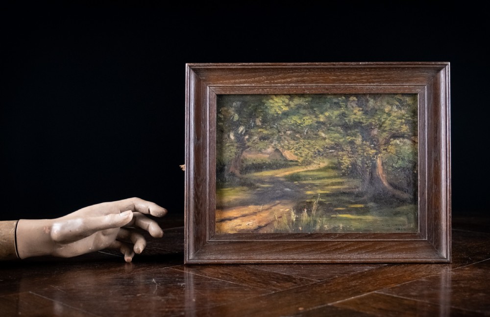 An early 20th-century oil painting on canvas depicting a shaded woodland path surrounded by dense green foliage, set within a dark molded wooden frame. View VI