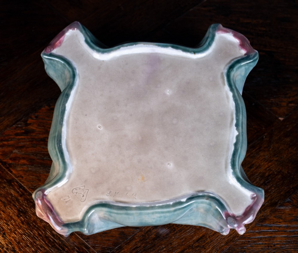 A square-shaped Art Nouveau glazed ceramic centre bowl featuring sculpted facial masks at each corner in soft green and iridescent pink glazes. View XIV