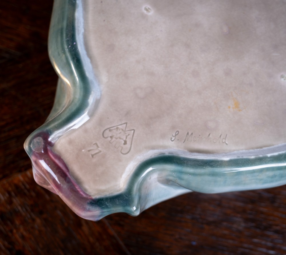 A square-shaped Art Nouveau glazed ceramic centre bowl featuring sculpted facial masks at each corner in soft green and iridescent pink glazes. View XV