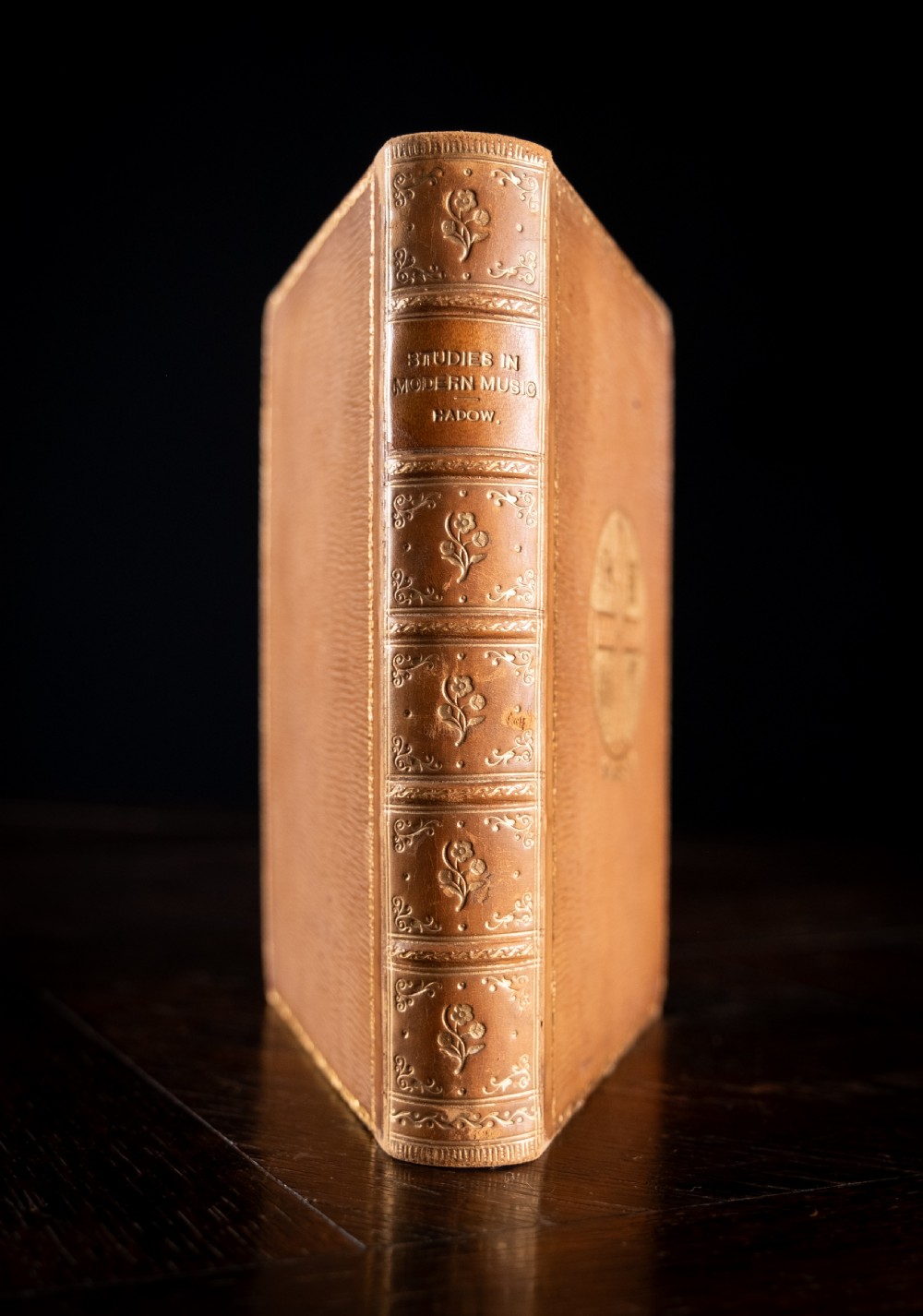 An upright 1898 tan leather-bound book featuring a gold-tooled decorative spine with floral motifs and raised bands.