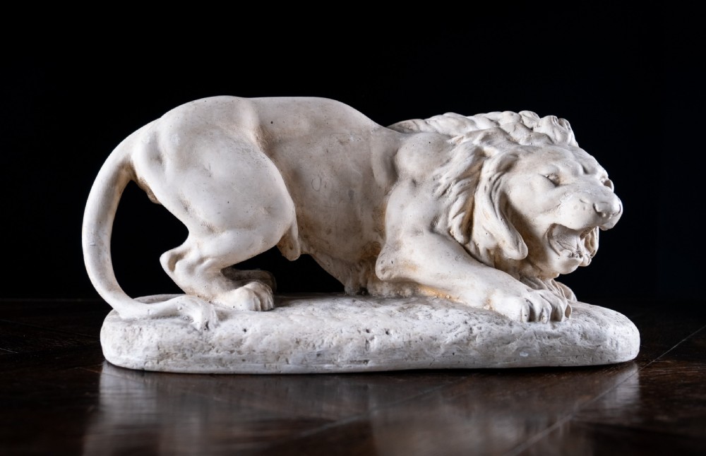 An off-white plaster sculpture depicting a prowling lion with an open mouth and detailed mane on an integral oval base.
