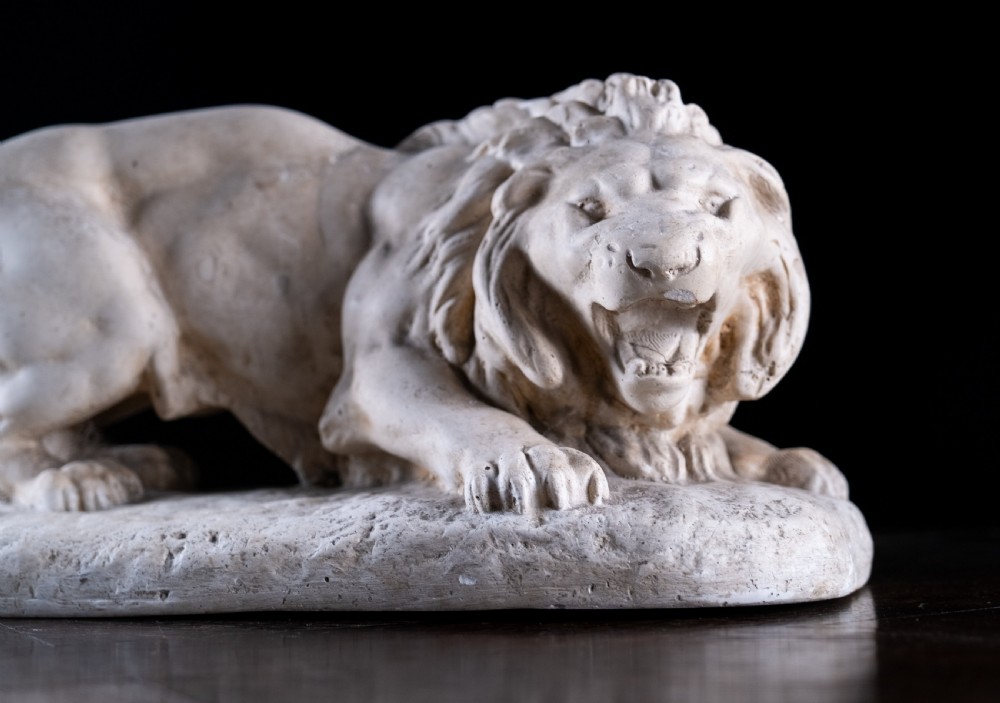 An off-white plaster sculpture depicting a prowling lion with an open mouth and detailed mane on an integral oval base. View II