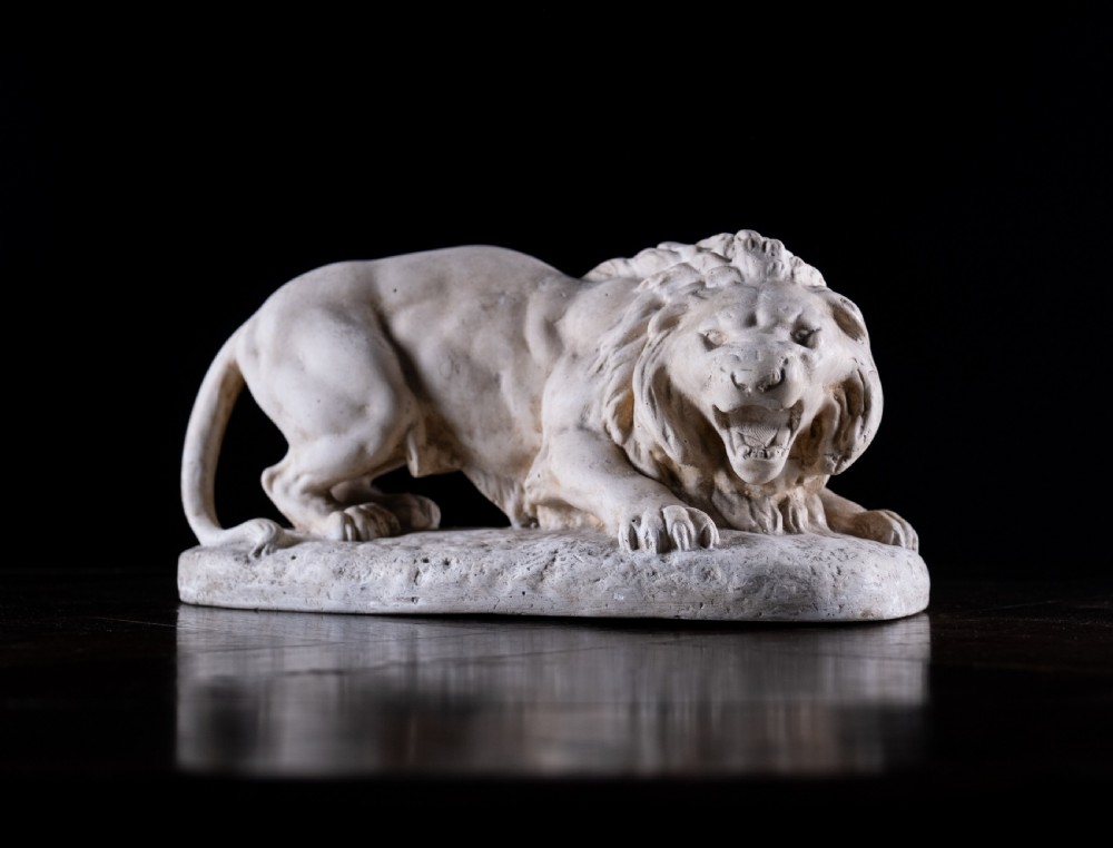 An off-white plaster sculpture depicting a prowling lion with an open mouth and detailed mane on an integral oval base. View III