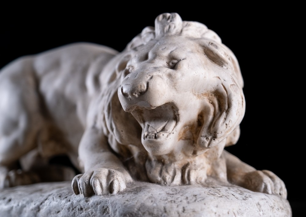 An off-white plaster sculpture depicting a prowling lion with an open mouth and detailed mane on an integral oval base. View IV