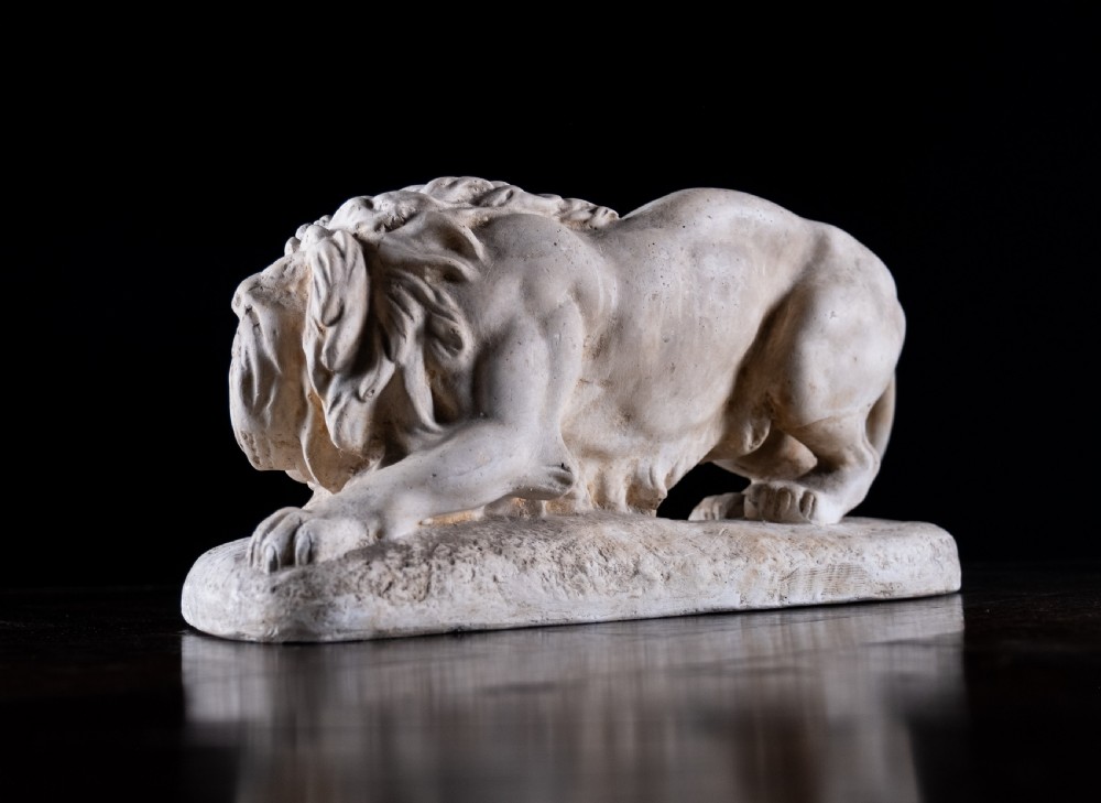 An off-white plaster sculpture depicting a prowling lion with an open mouth and detailed mane on an integral oval base. View VI