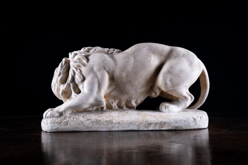 An off-white plaster sculpture depicting a prowling lion with an open mouth and detailed mane on an integral oval base. View VII