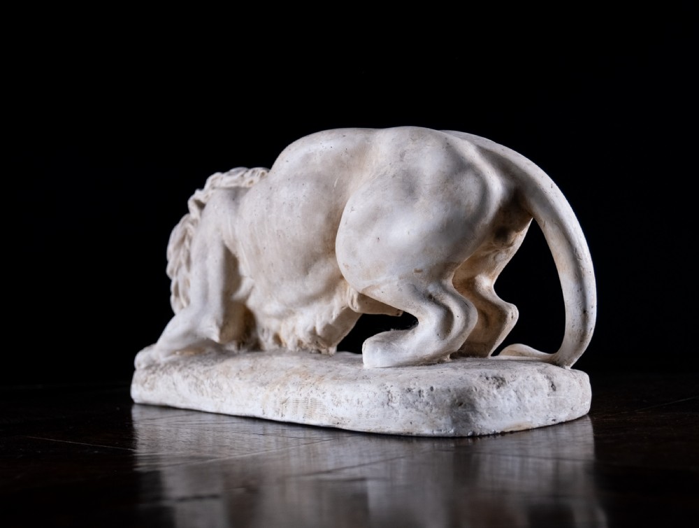 An off-white plaster sculpture depicting a prowling lion with an open mouth and detailed mane on an integral oval base. View VIII
