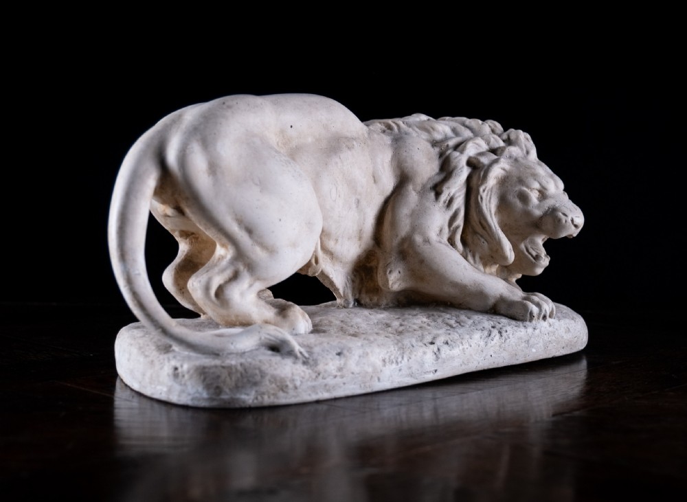 An off-white plaster sculpture depicting a prowling lion with an open mouth and detailed mane on an integral oval base. View IX