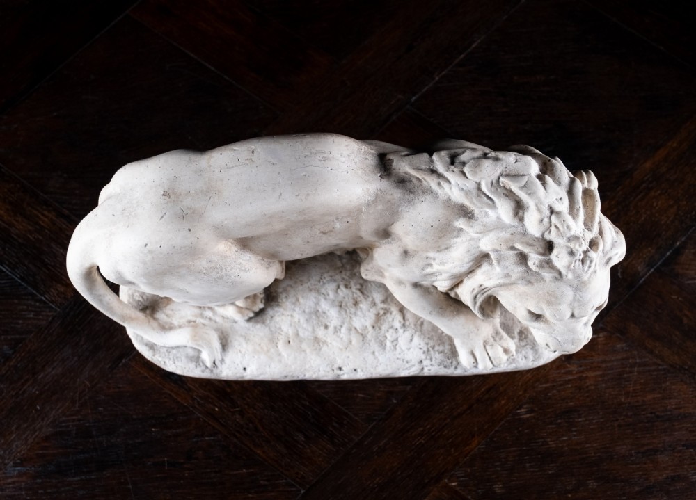 An off-white plaster sculpture depicting a prowling lion with an open mouth and detailed mane on an integral oval base. View XII