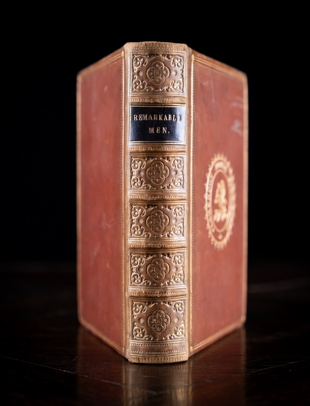 A Victorian tan leather-bound book titled Remarkable Men standing upright with ornate gold tooling on the spine and cover.