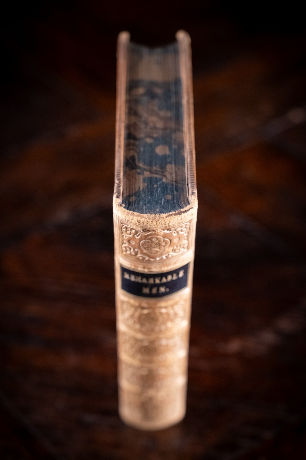 A Victorian tan leather-bound book titled Remarkable Men standing upright with ornate gold tooling on the spine and cover. View IV