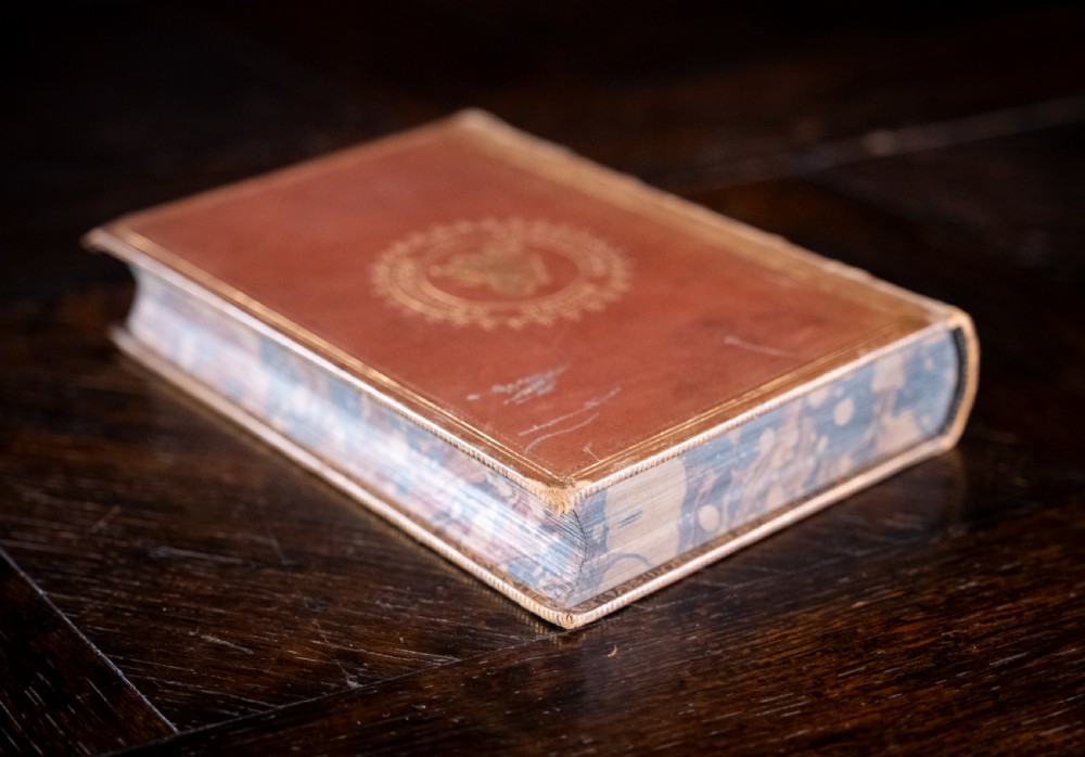 A Victorian tan leather-bound book titled Remarkable Men standing upright with ornate gold tooling on the spine and cover. View V