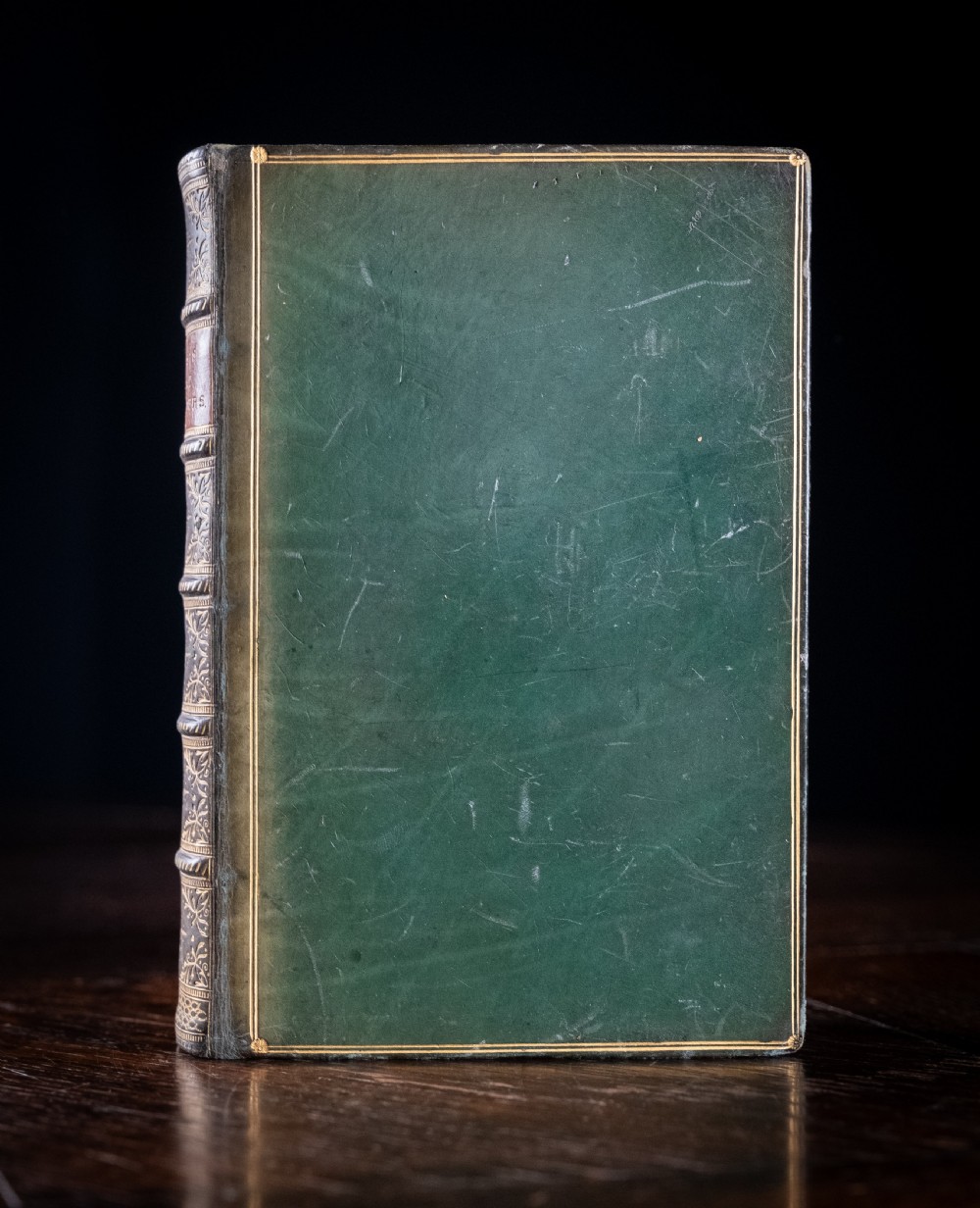 An antique Victorian book standing vertically, featuring green leather covers with gilt border lines and a dark brown spine detailed with gold-tooled compartments. View II