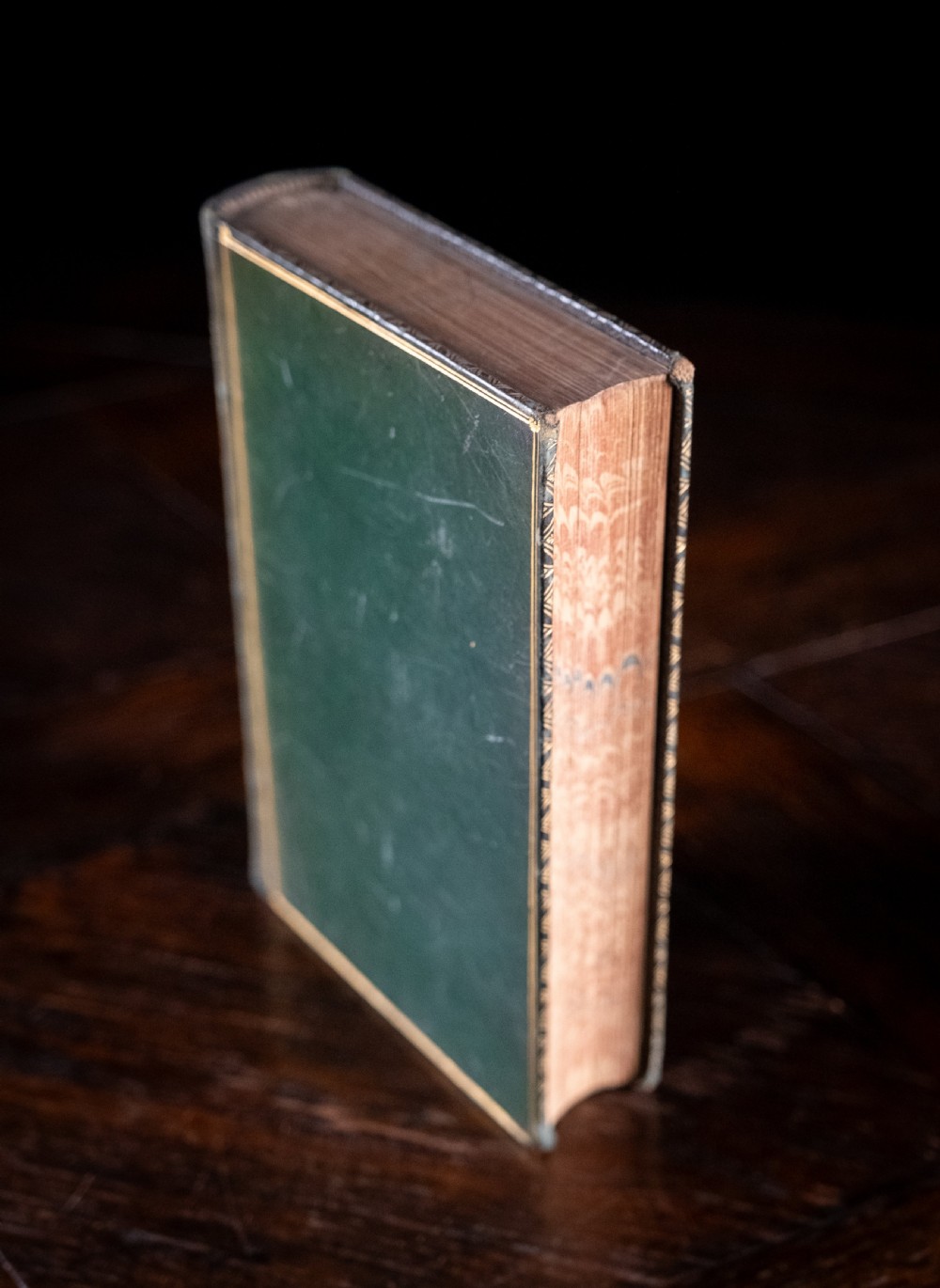 An antique Victorian book standing vertically, featuring green leather covers with gilt border lines and a dark brown spine detailed with gold-tooled compartments. View III