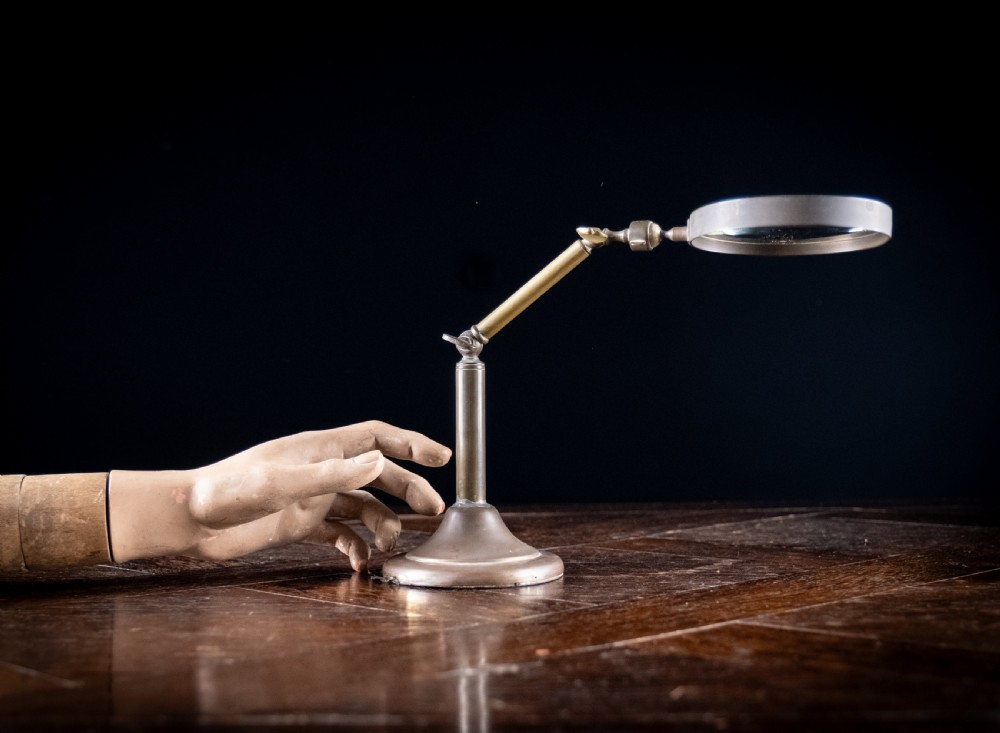 An antique Edwardian brass magnifying glass featuring an adjustable articulated arm and a circular weighted base.